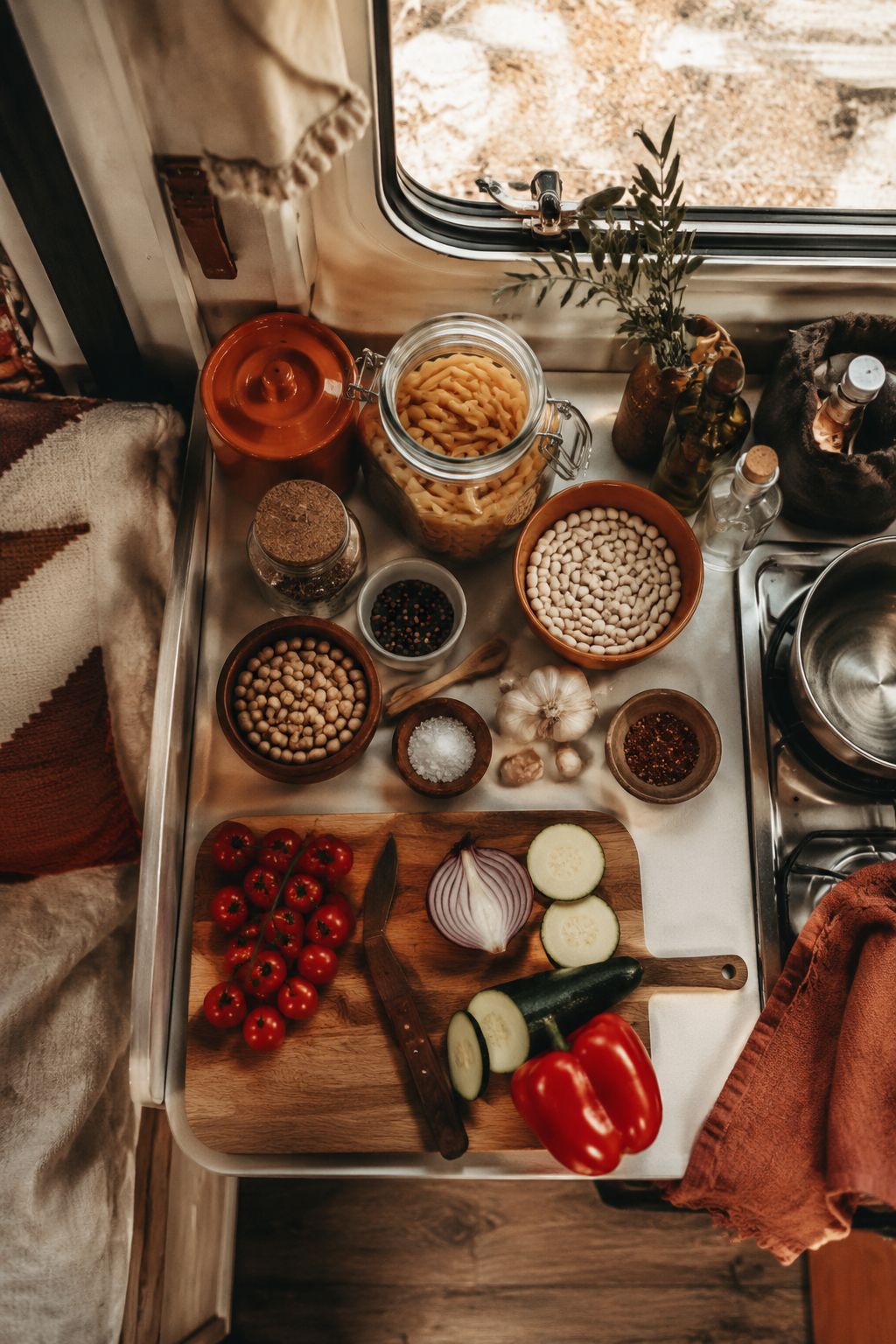 Portrait/Pinterest format () overhead flat-lay shot of a compact RV kitchen counter with organized meal prep ingredients:
