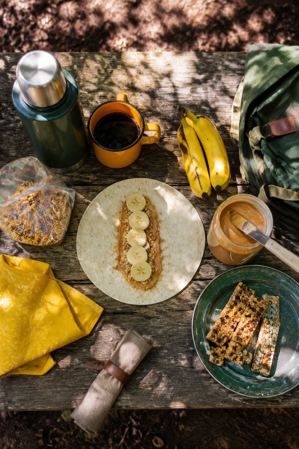 Portrait/Pinterest format () showing a top-down aerial view of a camp picnic table with multiple breakfast items: a burrito