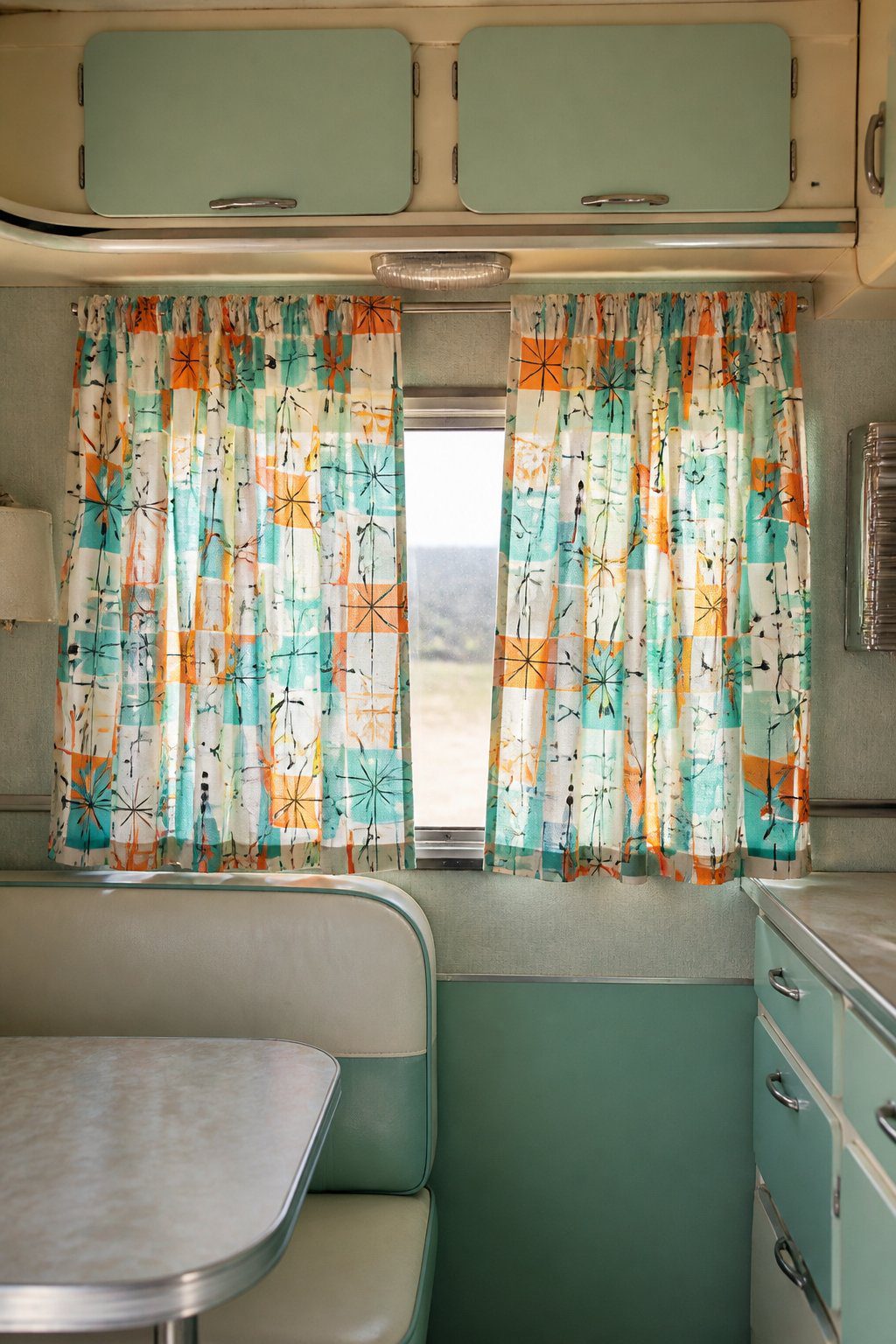 Turquoise and orange patterned curtains hang inside a cozy vintage camper.