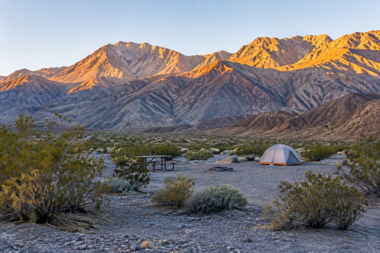 A quiet campsite with a tent and picnic table beneath rugged desert mountains.